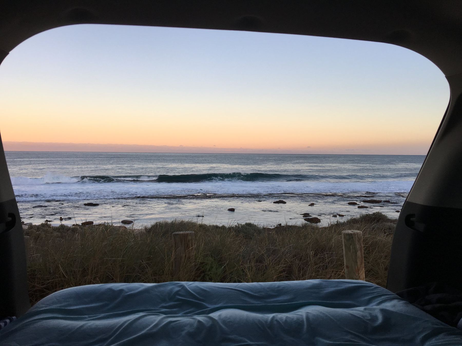 Blick aus dem Bett eines Campervans auf die Brandung bei Sonnenuntergang